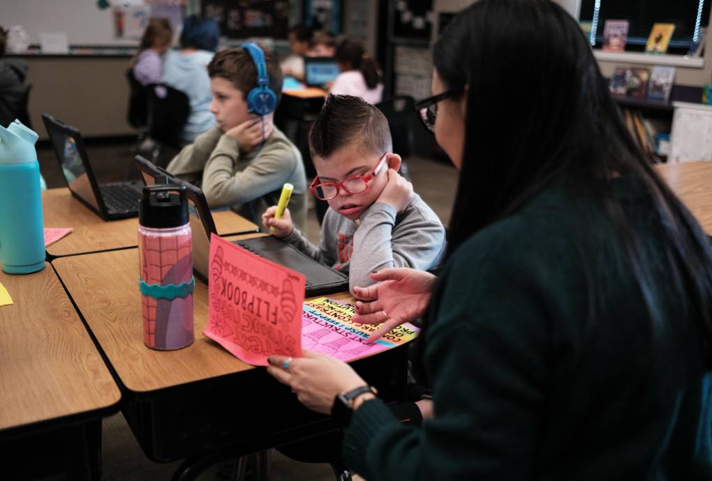 Two students at their desks learn from a teacher.