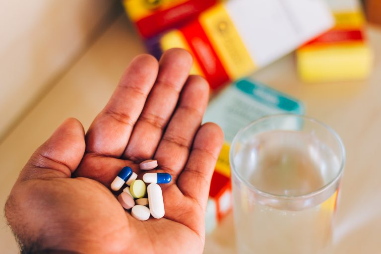 Mão segurando vários tipos de medicamentos e um copo d´água