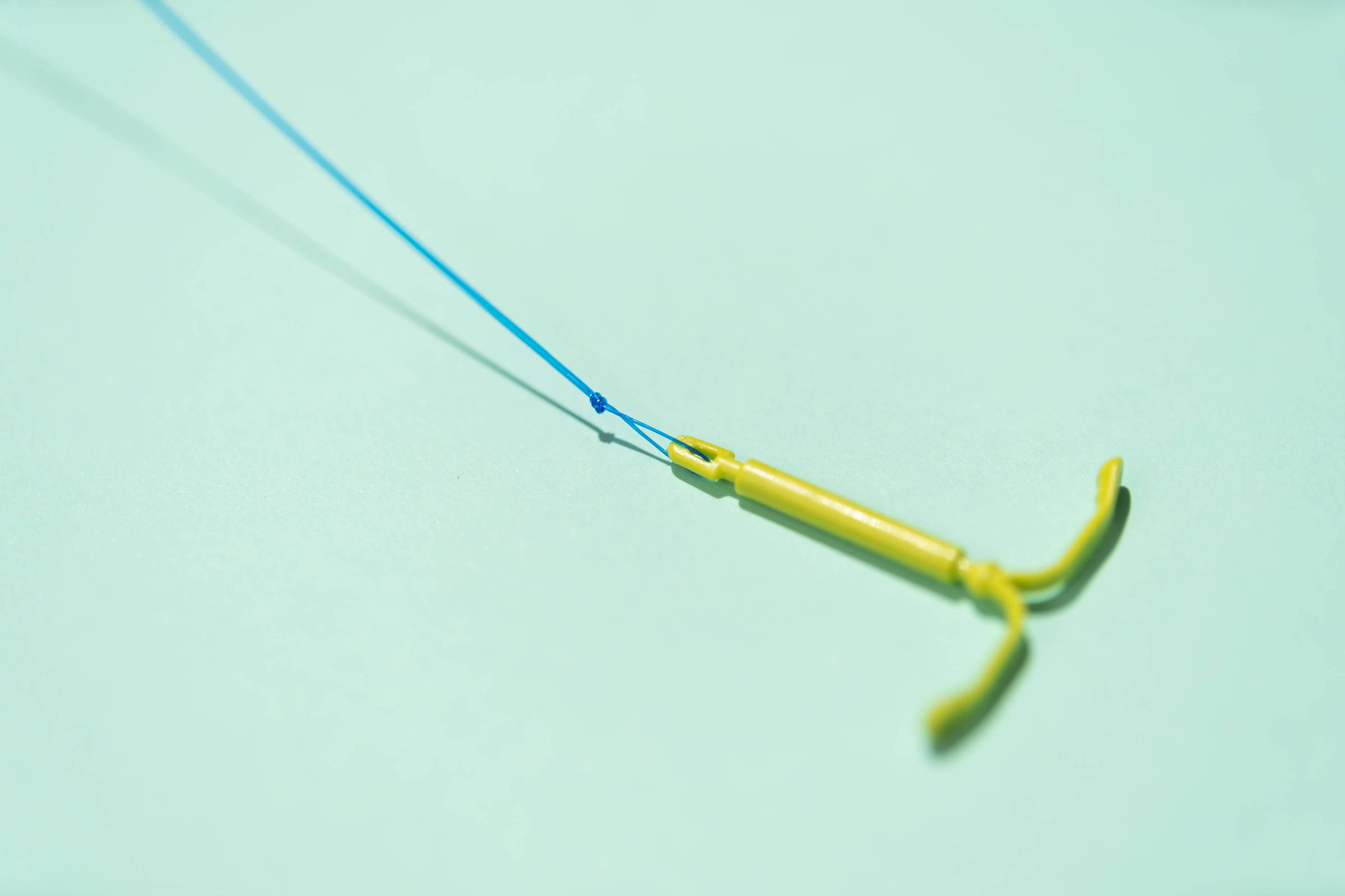 A imagem mostra um equipamento de pesca, com um corpo amarelo e uma linha azul. O corpo tem uma forma alongada e termina em duas extremidades que se curvam para cima.