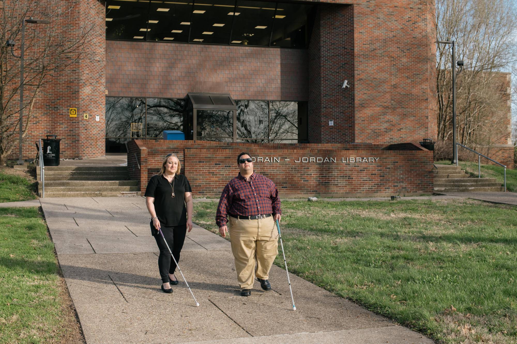 Two people who are blind are walking on the campus of West Virginia State University while holding canes.