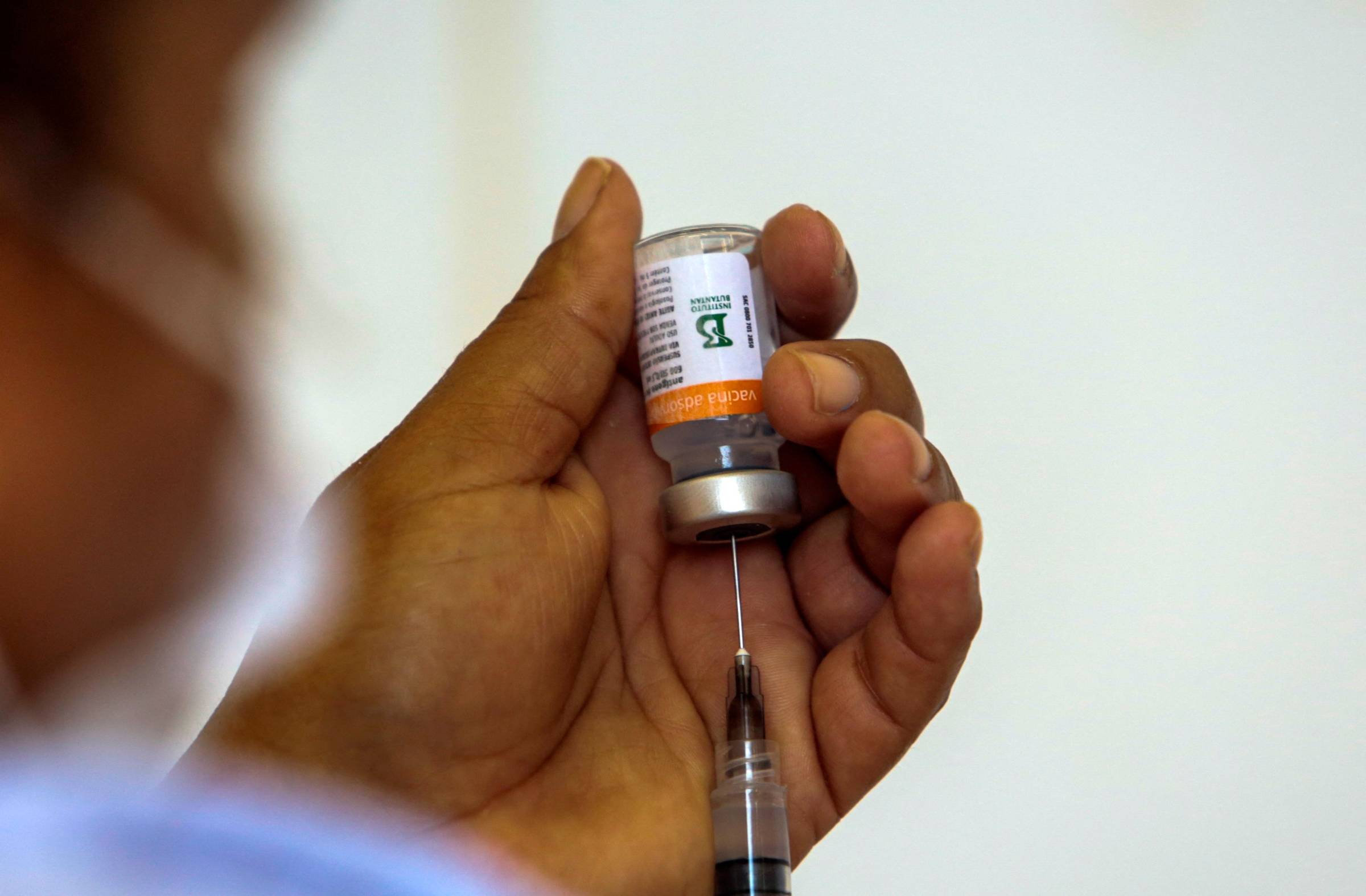 Imagem mostra profissional de saúde manueseando frasco da Coronavac