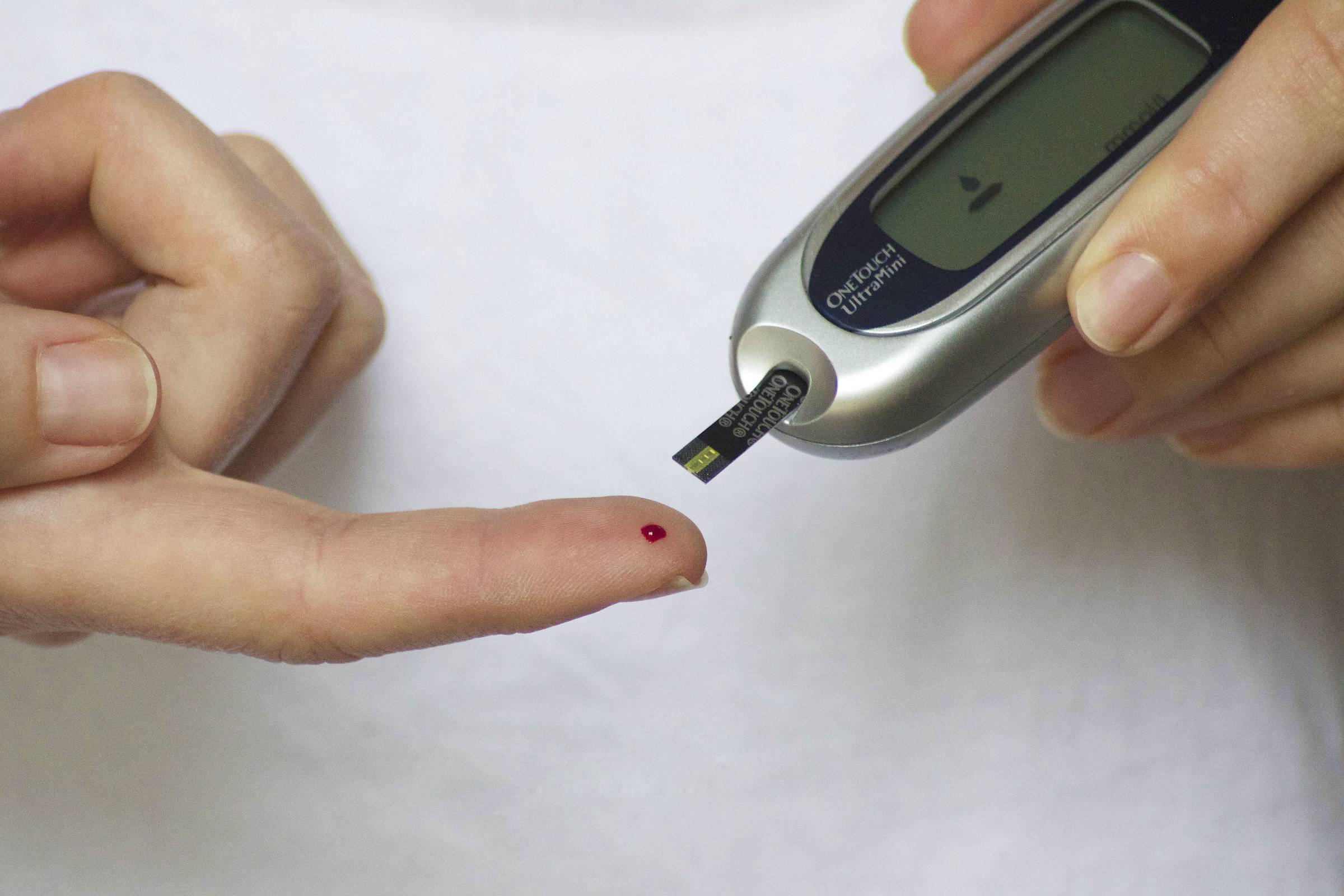 Um dedo furado, com uma gota de sangue e, ao lado, um aparelho que mede a glicose