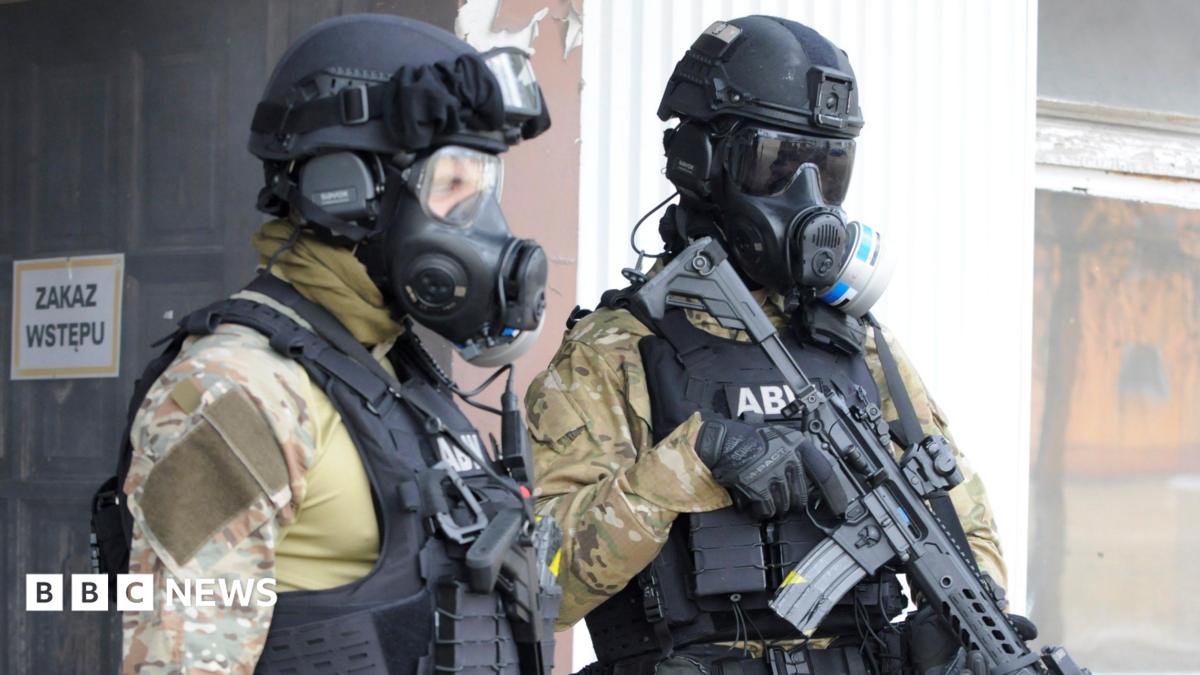 Two men wear gas masks and military uniform and carry guns