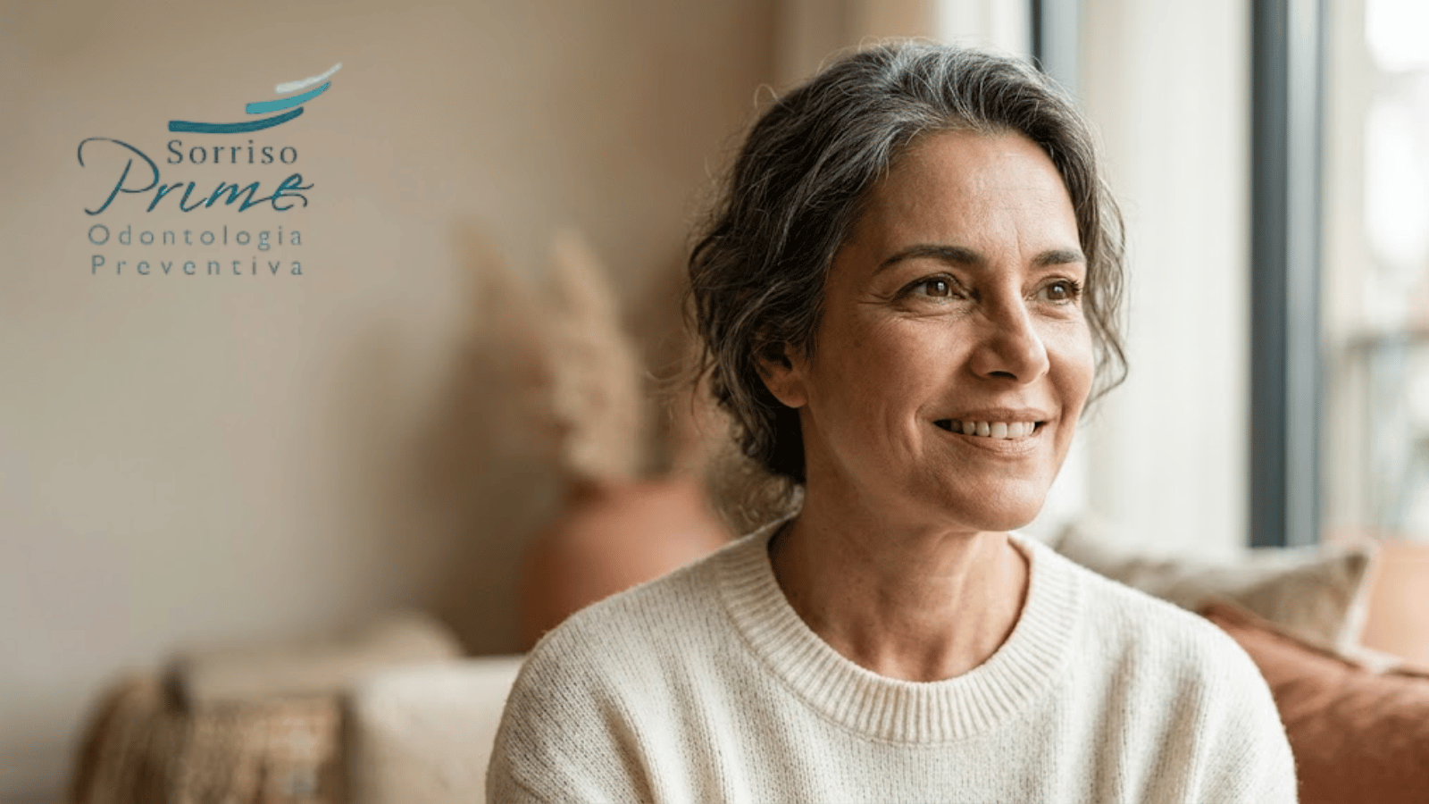 Mulher madura sorrindo naturalmente em ambiente acolhedor, representando saúde bucal, bem-estar, autonomia e qualidade de vida.